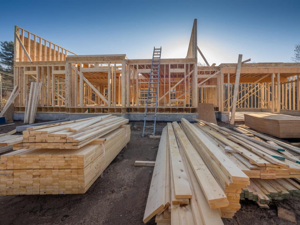 A large pile of timber on a construction site with framing in the background