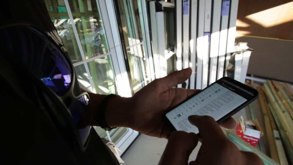 A builder uses a mobile phone to check his to-do list using Buildxact.