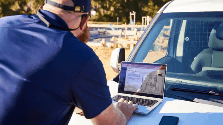 Residential builder reviewing construction drawings on a laptop while preparing a construction takeoff at a job site