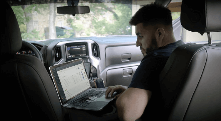 Residential builder reviewing construction job data on a laptop from a vehicle at the job site.