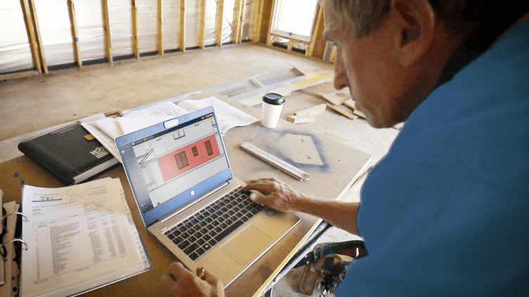 Contractor reviewing digital construction drawings and documents on a laptop at a residential job site before starting work.