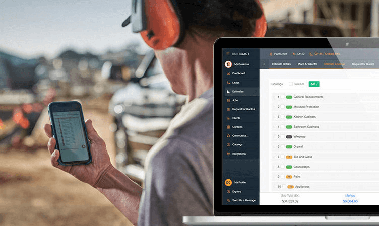 Residential builder on a construction site holding a mobile phone, with an overlay showing the Buildxact estimating interface listing cost categories such as cabinetry, drywall, paint, and appliances with subtotal and markup displayed on a laptop screen.
